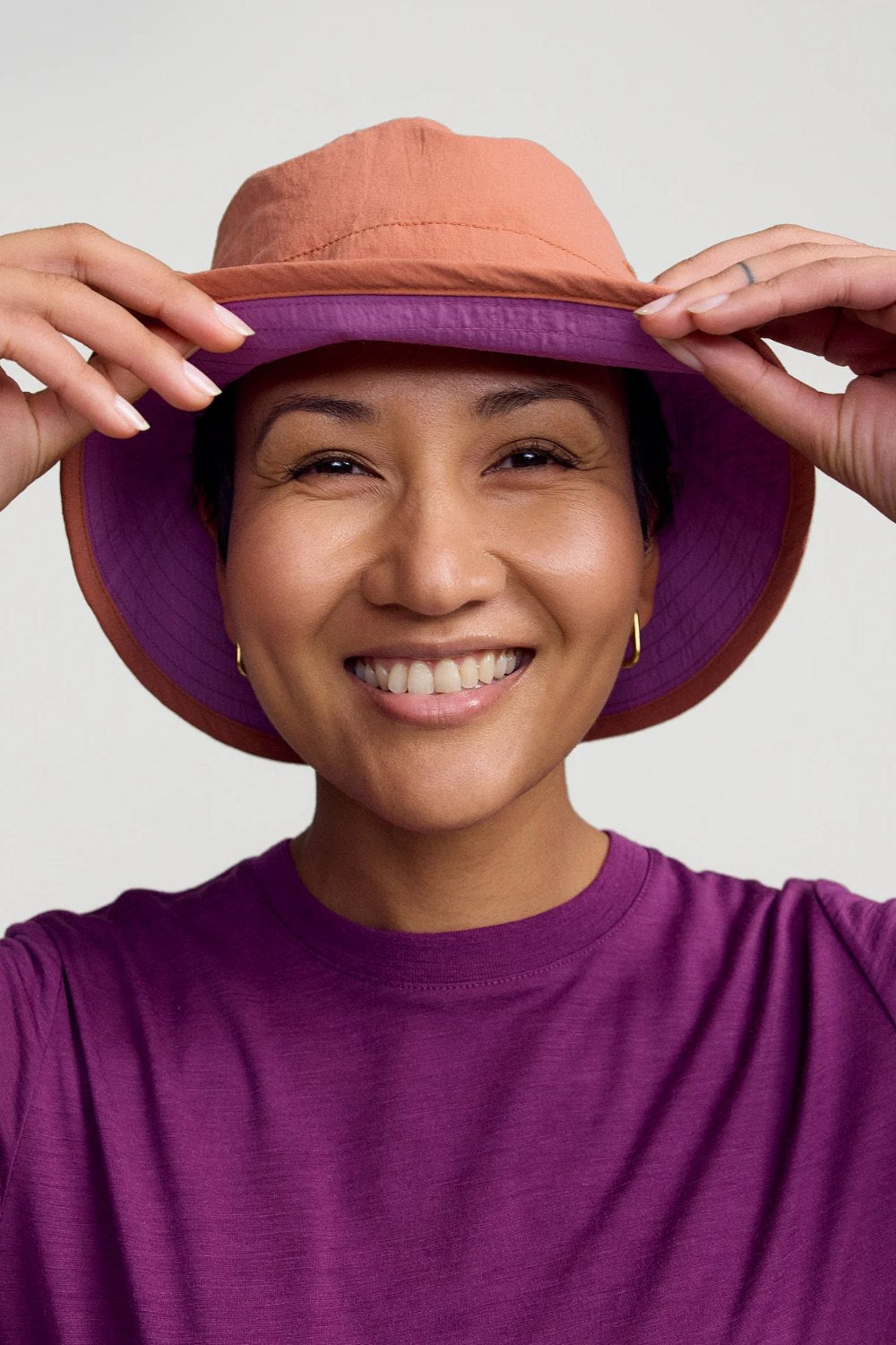 Femme souriante portant un bob anti-UV - Ridge, réversible avec tissu UPF 50+, style décontracté.