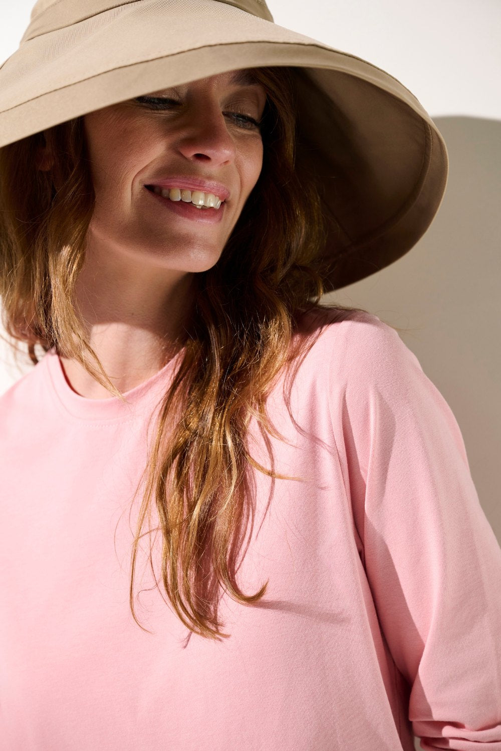 Femme souriante portant un chapeau anti-UV - Faro beige et un t-shirt rose, protection solaire UPF 50+.