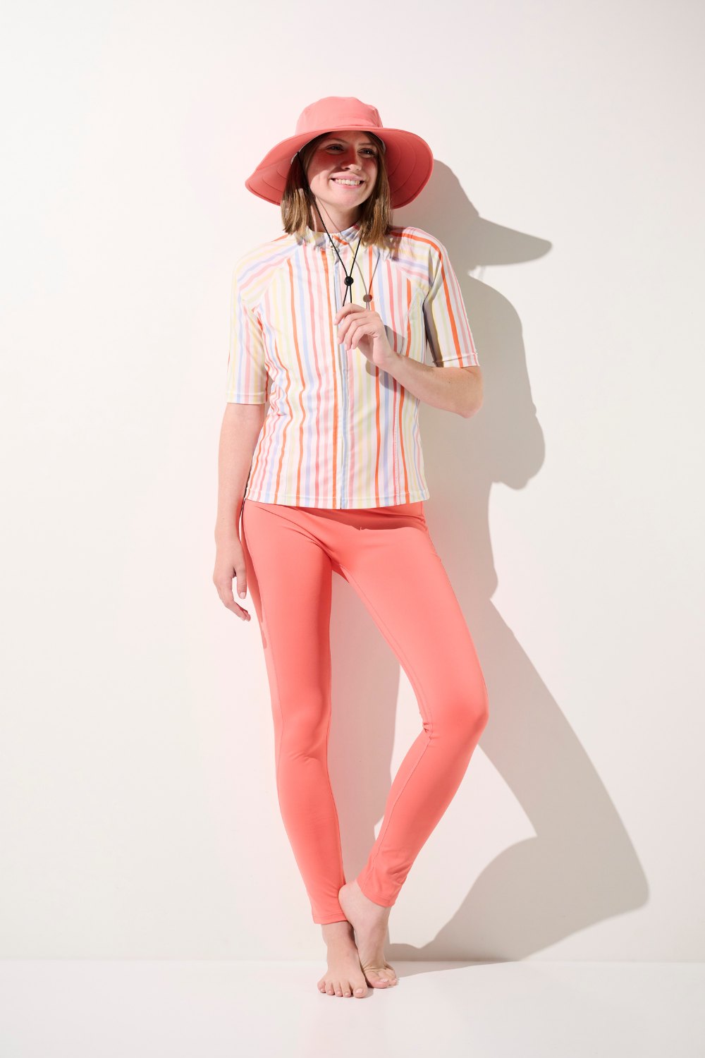 Chapeau de bain anti-UV - Galápagos rose porté par femme, associé à un maillot léger UPF 50+ et pantalon, parfait pour le soleil.