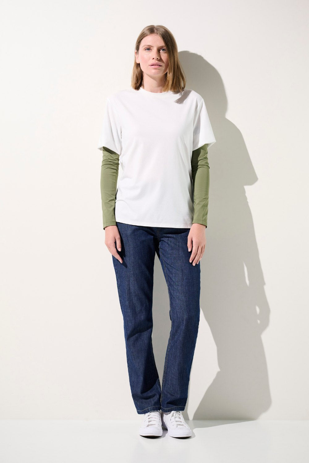 Femme portant un t-shirt blanc avec des manches anti-UV Gobi vertes, idéal pour la protection solaire.