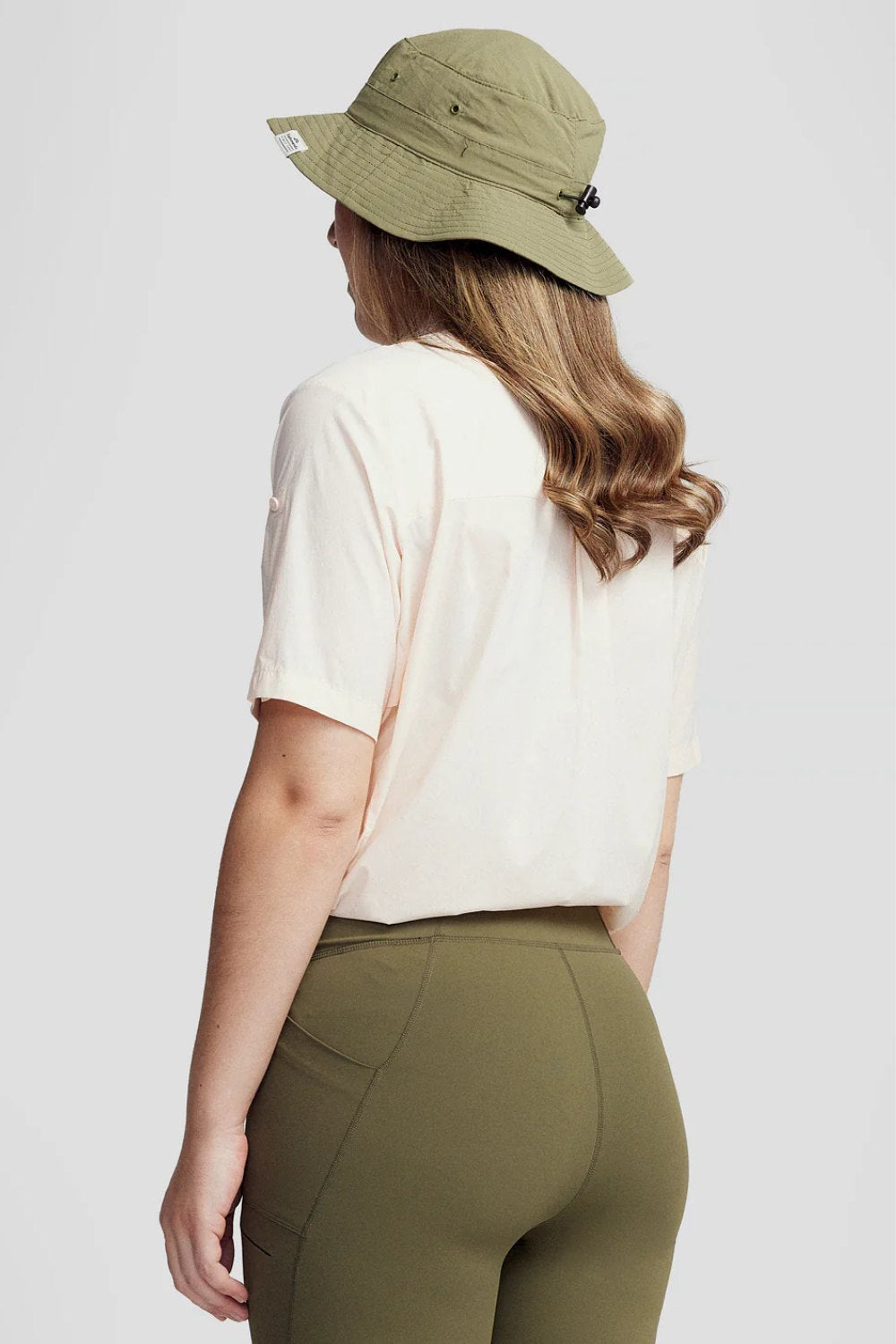Femme portant une chemise anti-UV - Ridge beige UPF 50+, pantalon de sport et chapeau, idéale pour les randonnées.