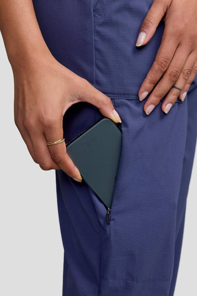 Pantalon anti-UV Miro en bleu avec poche pratique, femme mettant son téléphone dans la poche.