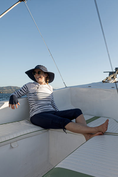 Femme en T-shirt de bain anti-UV - Moorea, rayé, UPF 50+, se détendant sur un bateau au soleil.